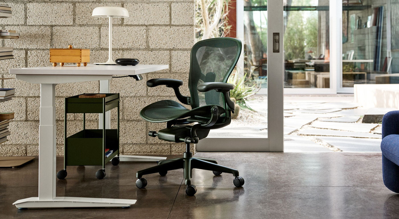 A Jasper green Herman Miller Aeron desk chair as part of a bright home office featuring a white Jarvis sit stand desk and olive green OE1 storage trolley.