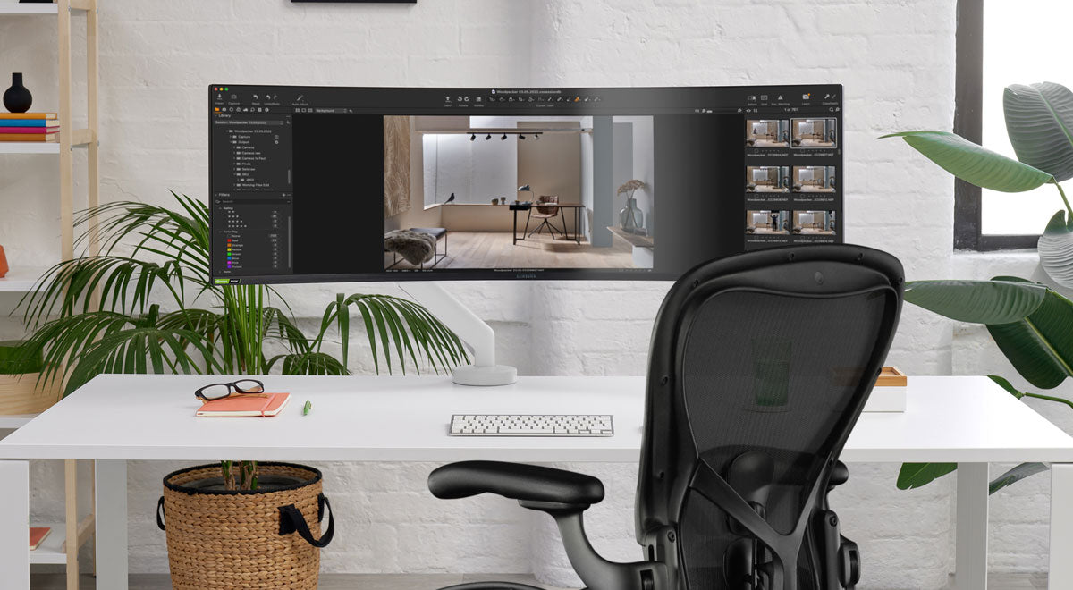 Front view of a white Flo X monitor arm by CBS attached to a white desk, positioned in front of a black Aeron office chair by Herman Miller.
