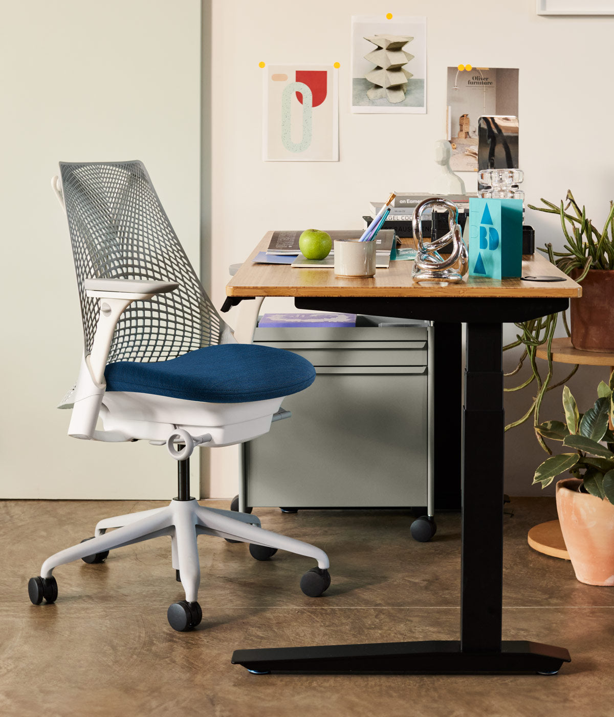 Home office scene containing Jarvis sit-stand desk with black legs and wood top alongside Sayl office chair in alpine white with blue seat pad