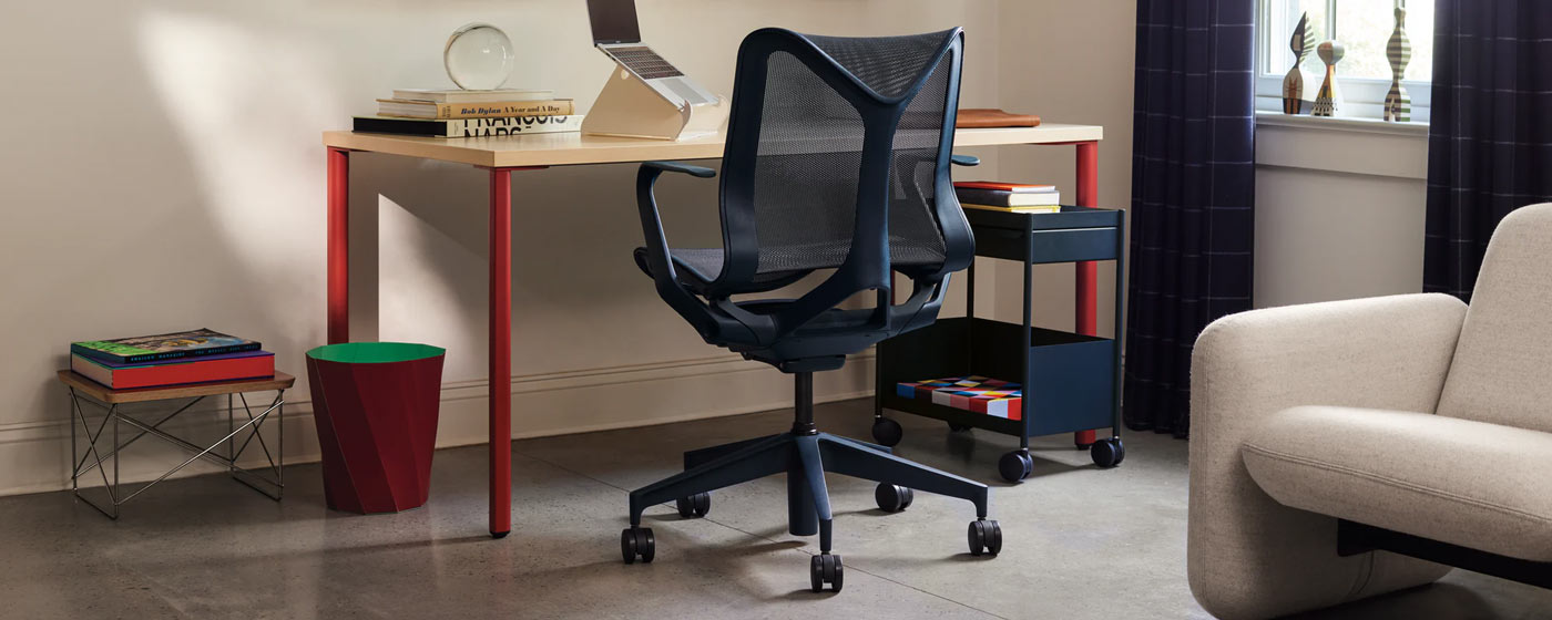 A blue Cosm office chair by Herman Miller, positioned in front of a red and ash OE1 desk by Herman Miller. Set in a home office, accessoriesed with a blue OE1 trolley, white Oripura laptop stand and red HAY Paper paper bin.