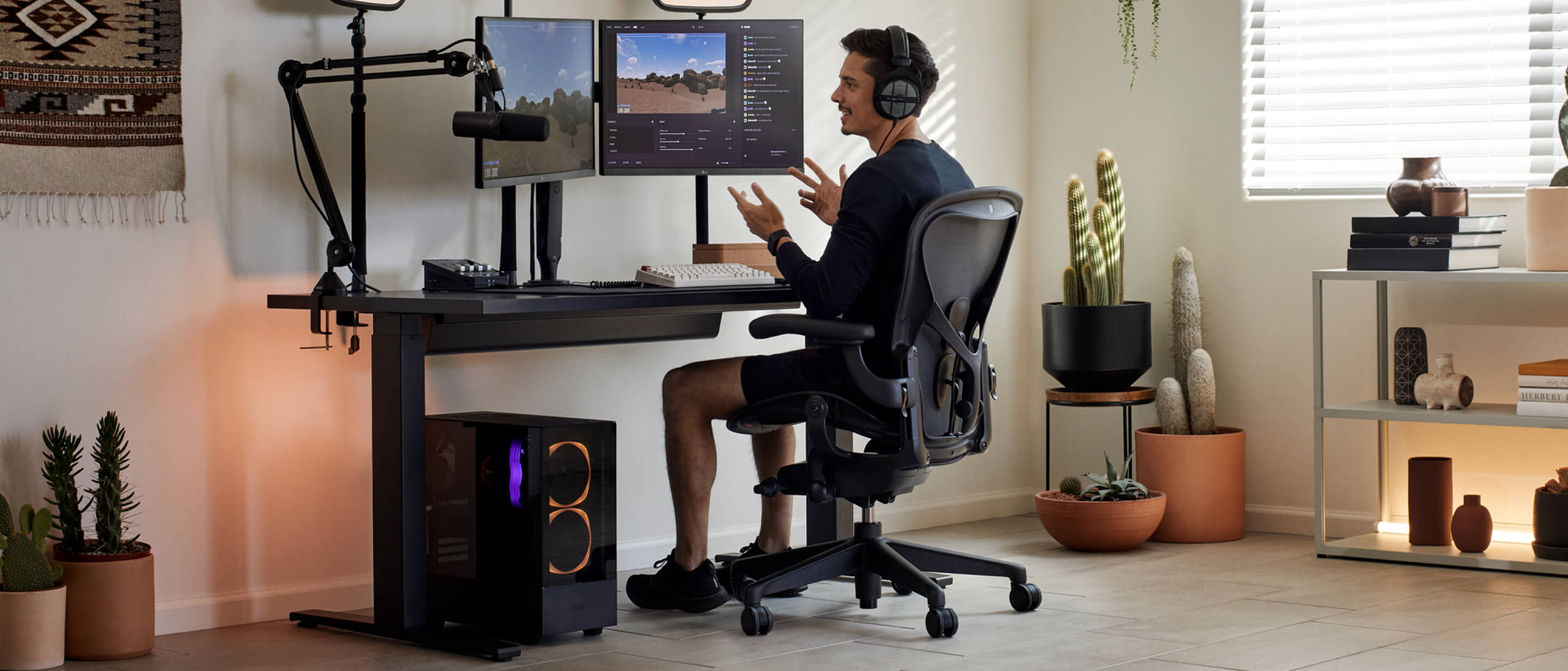 Gamer Xaryu with hands in air playing game at his Herman Miller set up in Aeron gaming chair with Nevi gaming desk and Ollin dual monitor arms