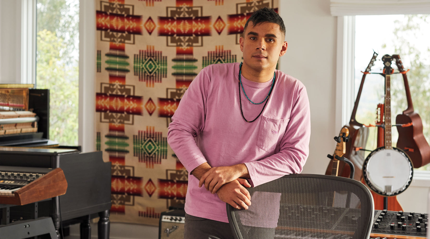 Rostam, musician, producer and composer, stood leaning on Aeron office chair in graphite with musical instruments in the background.