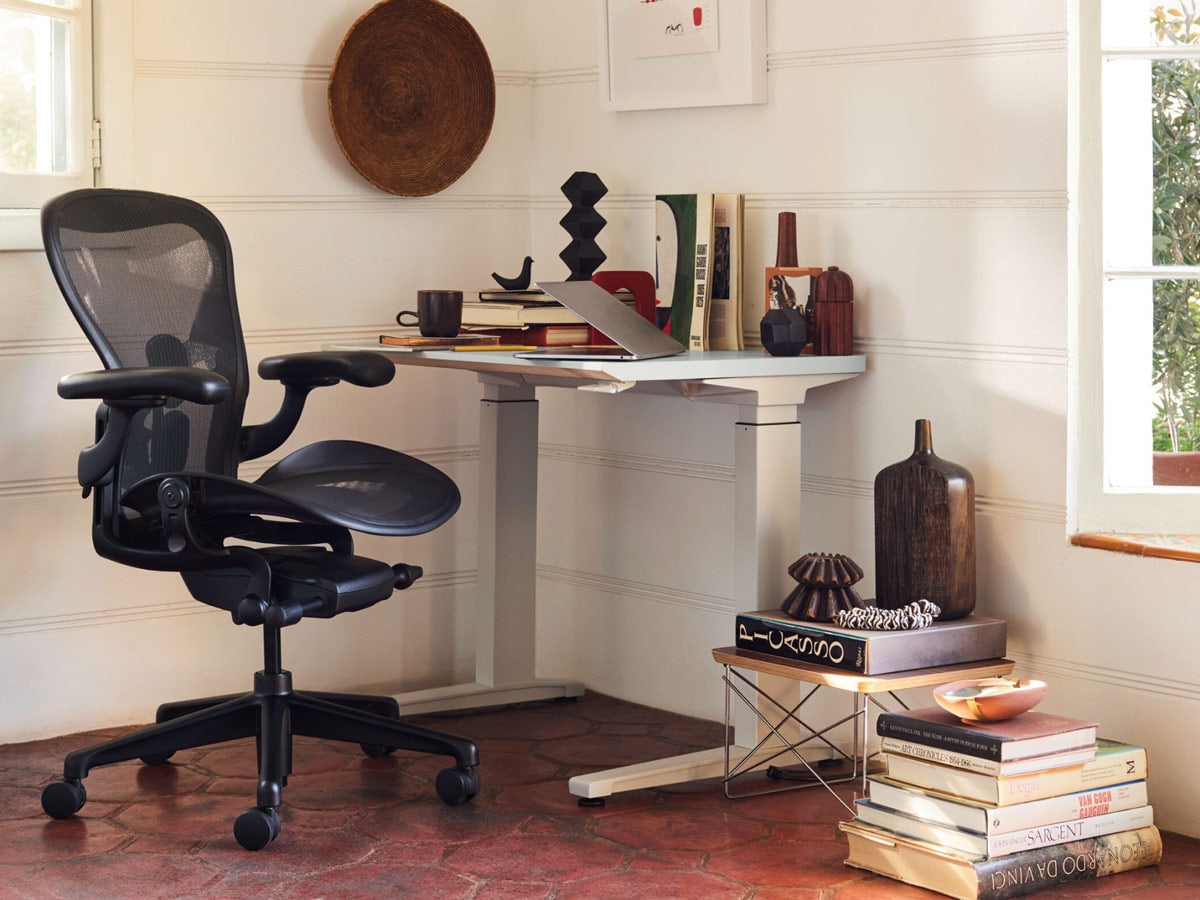 An ergonomic and personalized home office in a brightly lit corner, decorated with vases and books - featuring a Herman Miller Aeron desk chair.