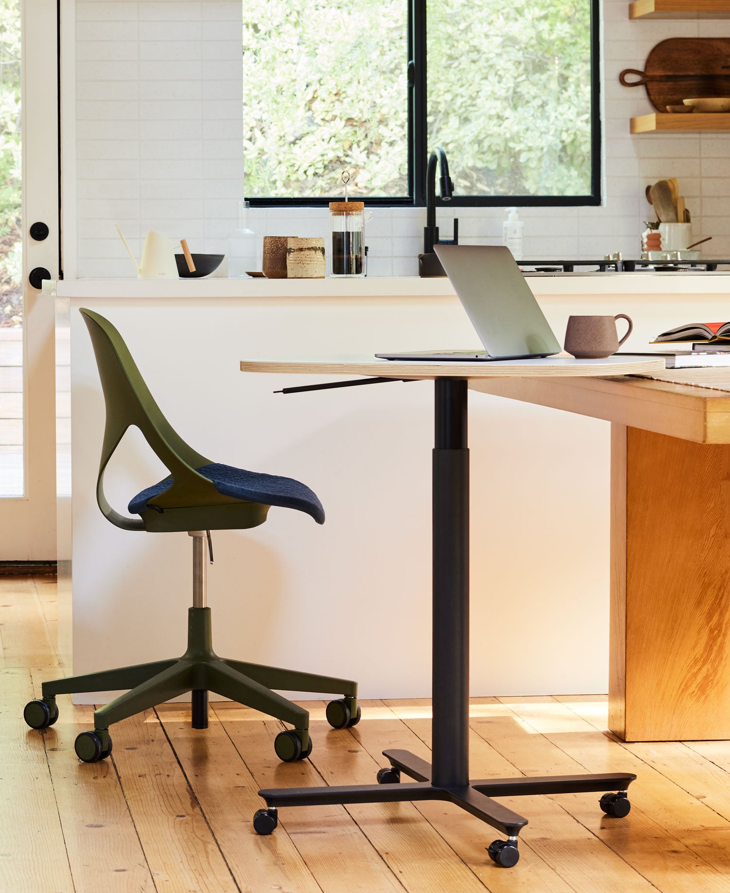 Photo set in a home kitchen with Zeph office chair in olive with midnight blue seat pad along with compact hieght adjustable Passport work table