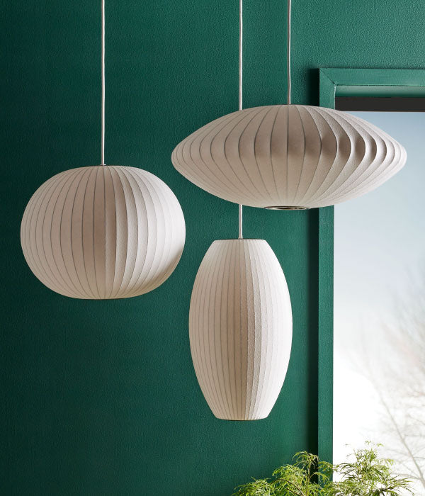 Three Nelson Bubble Pendant light shades in round, tall and saucer shapes against a deep green wall.