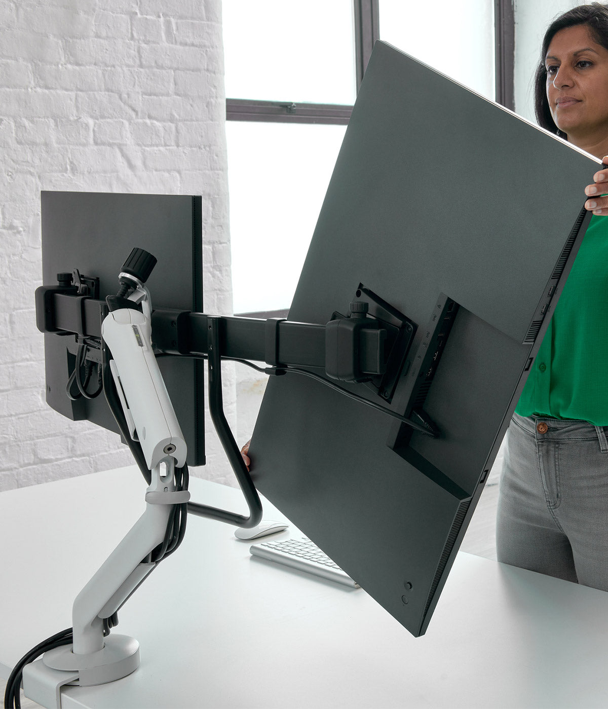 A CBS Flo X large format monitor arm holding two screens as a user adjusts the orientation.