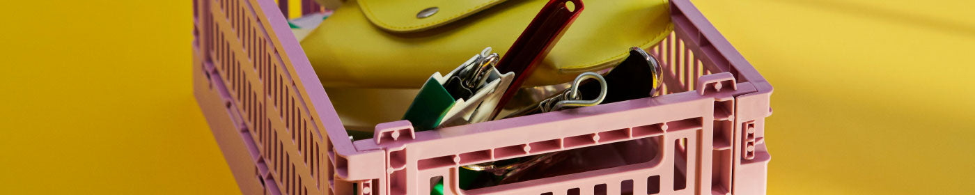 A soft pink storage crate containing a selection of objects against a yellow backdrop.