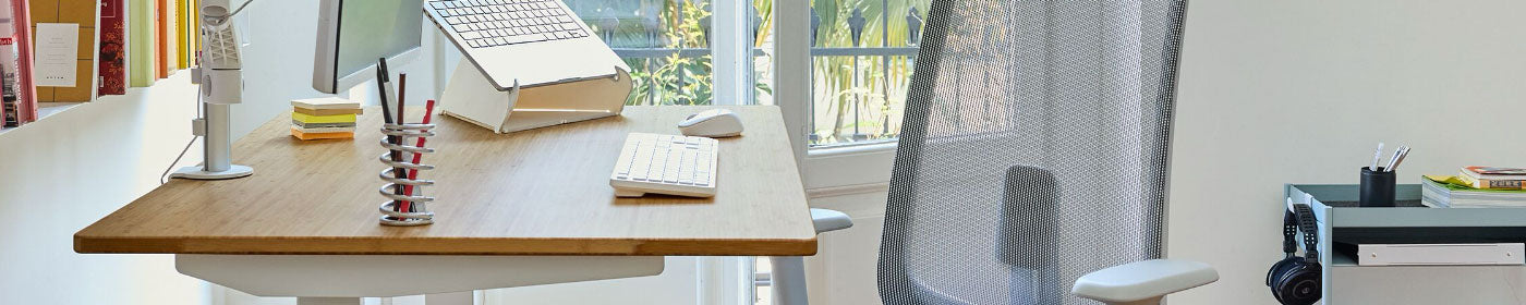 A bamboo desk with a white Lima monitor arm and Oripura laptop stand alongside a Herman Miller Verus chair and blue OE1 storage trolley.