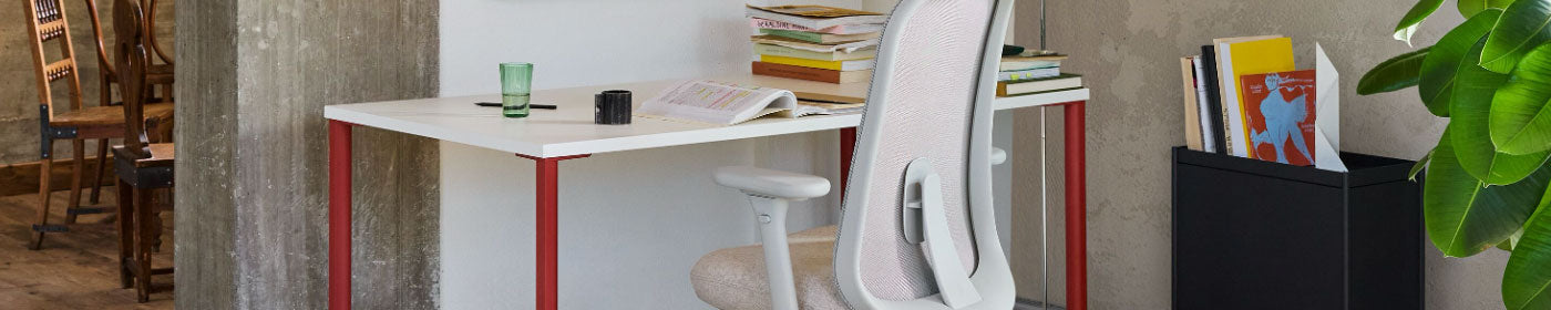 An OE1 desk with a white top and red legs as part of a home office setup with a pale Herman Miller Lima ergonomic office chair.