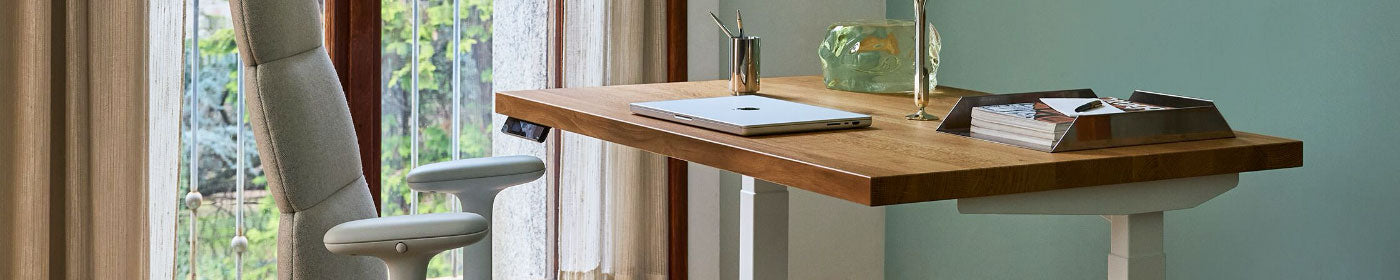 A soft grey Herman Miller Asari chair alongside a solid wood topped Jarvis sit stand desk as part of a home office.