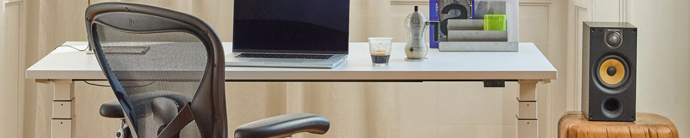 A white Nevi sit stand desk as part of a bright home office alongside a graphite Herman Miller Aeron ergonomic office chair.