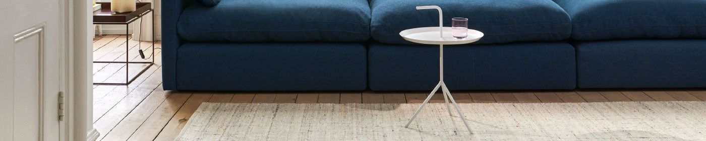 HAY DLM and Tray side tables in white and brown alongside a navy blue sofa as part of a living room setup.