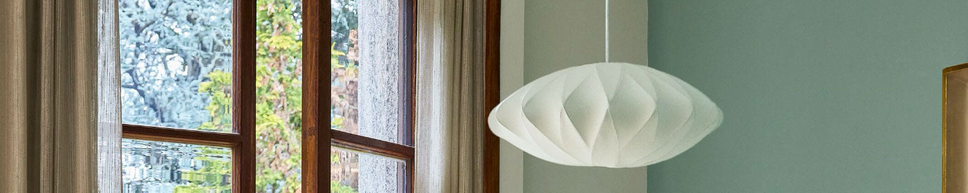 A criss-cross Nelson saucer bubble lamp light shade hanging in a bright room near an open window.