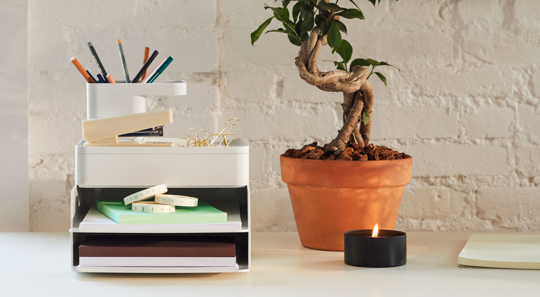 A set of concrete grey Formwork desk tidy accessories alongside a plant and candle on a desk.