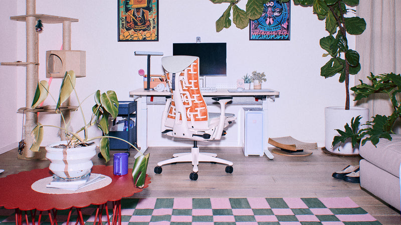 A white and orange Herman Miller Embody gaming chair with grey upholstery in a brightly lit living room PC gaming setup.