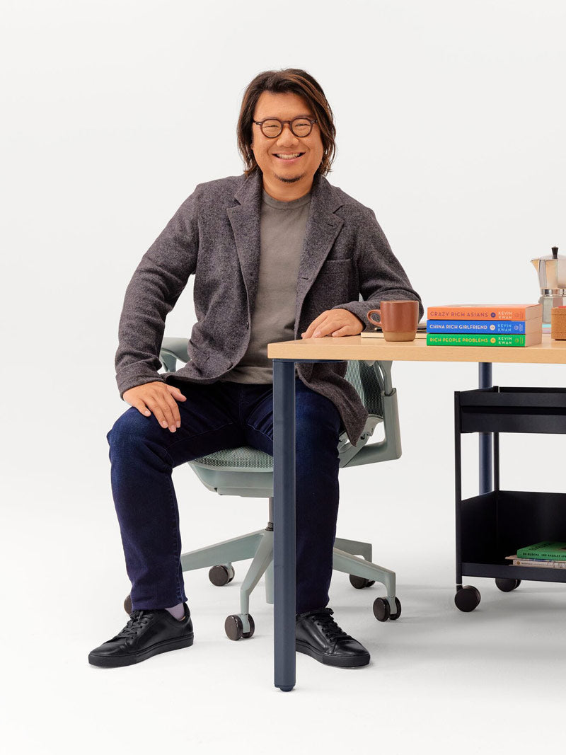 Cheerful photograph of Kevin Kwan sat in Glacier grey Cosm office chair leaning on an fixed height OE1 desk with nightfall legs and light ash top