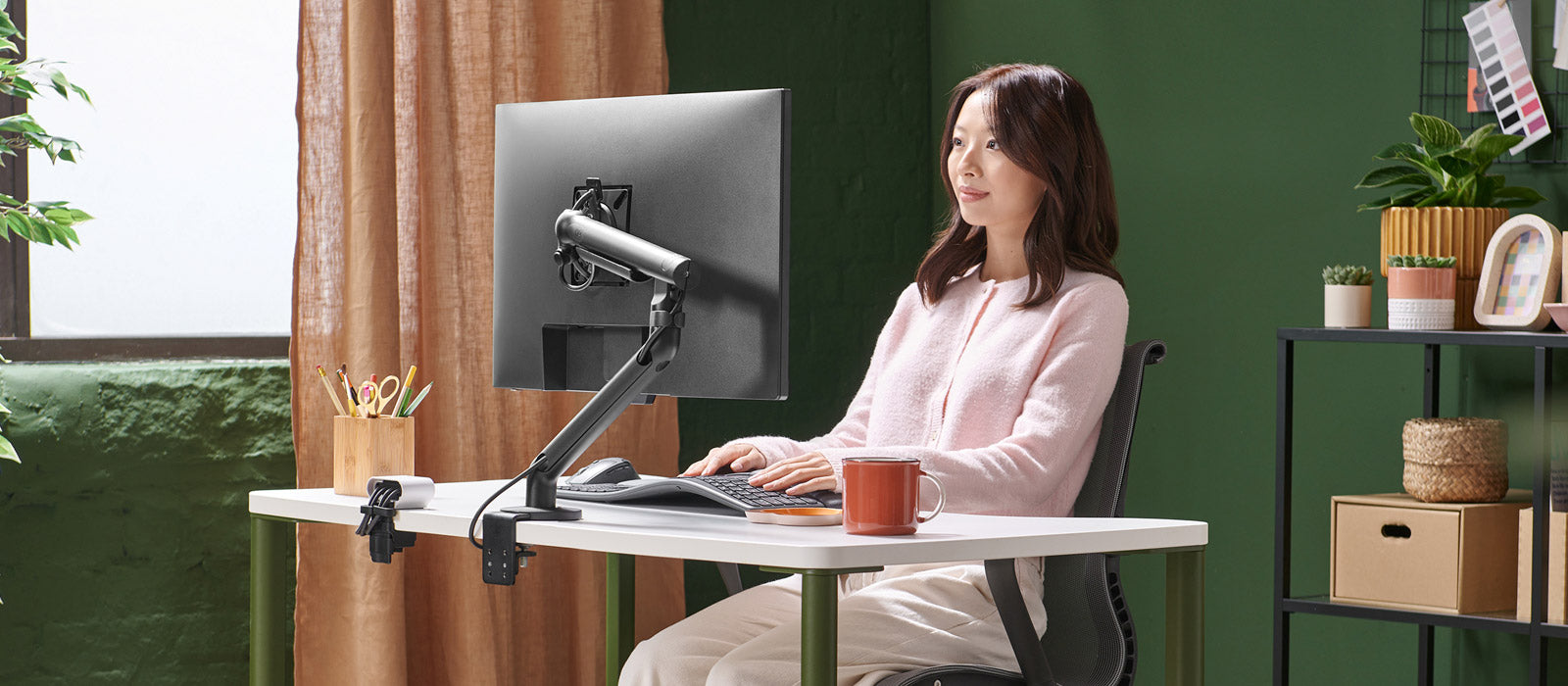 A woman sat at a Herman Miller OE1 desk working on a screen supported by a black Flo monitor arm.