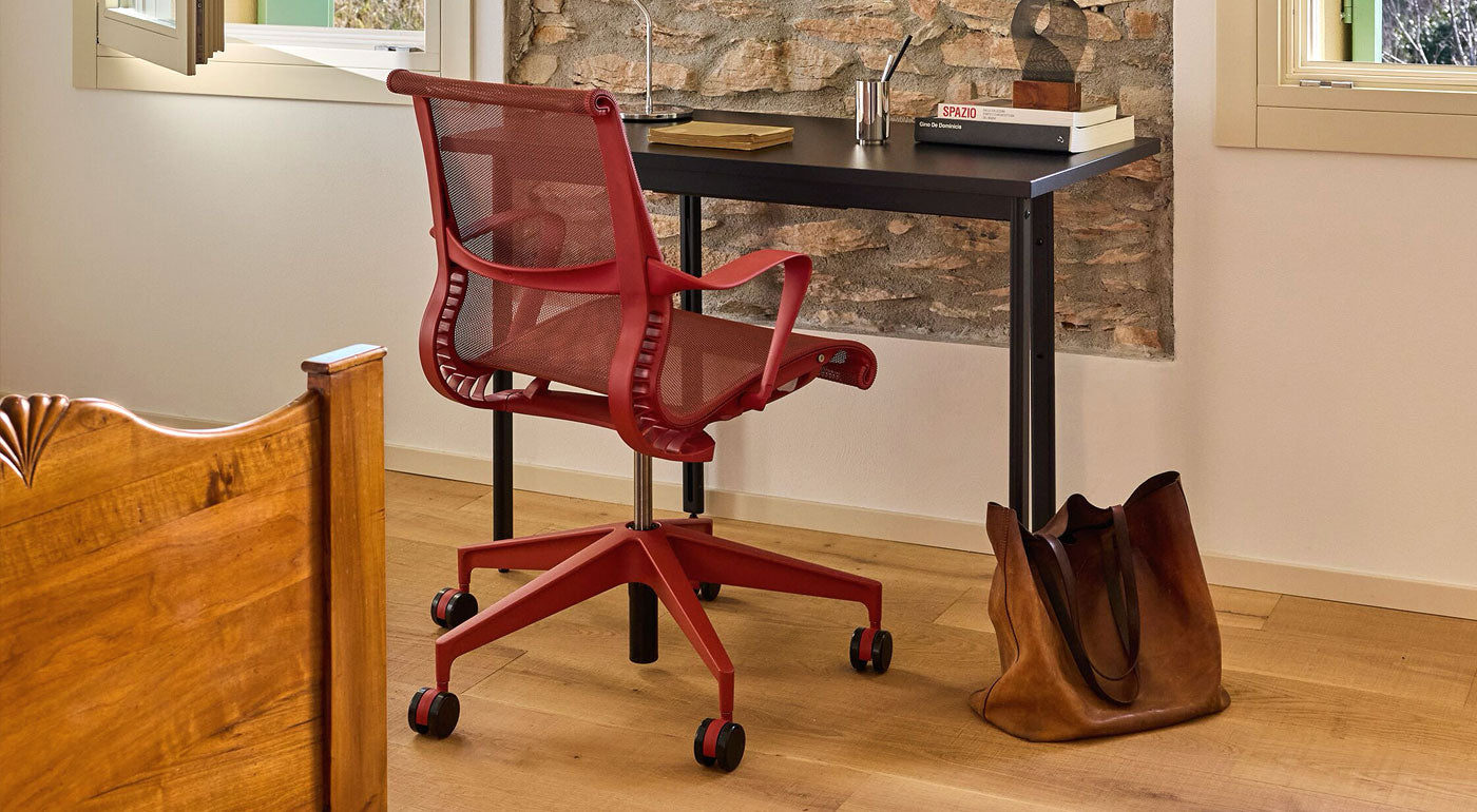 A canyon red Herman Miller Setu mesh ergonomic desk chair as part of a warm and bright bedroom home office.