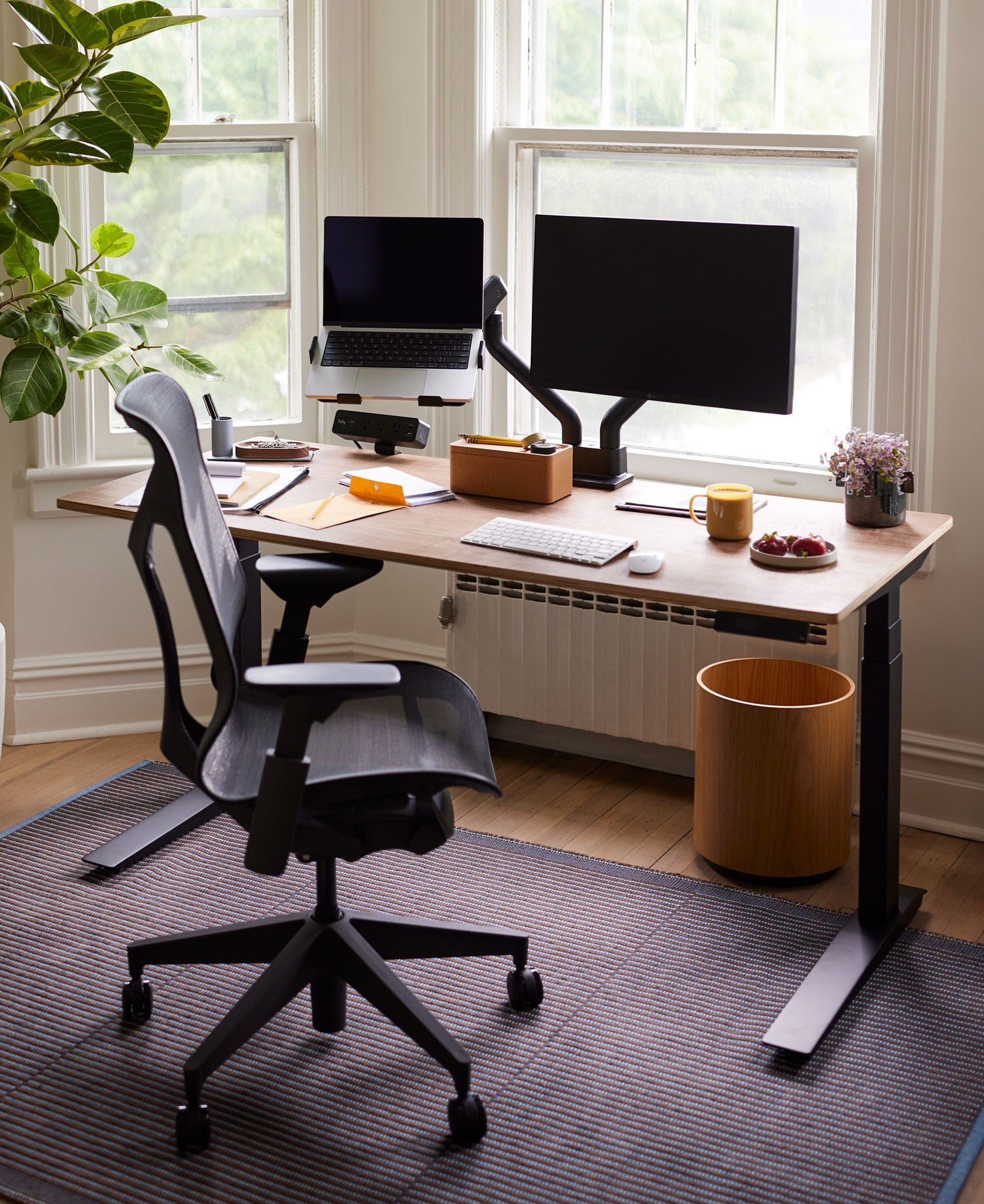 Home office setting with mid back Cosm office chair in graphite in front of Jarvis sit-stand desk with black legs and wooden top