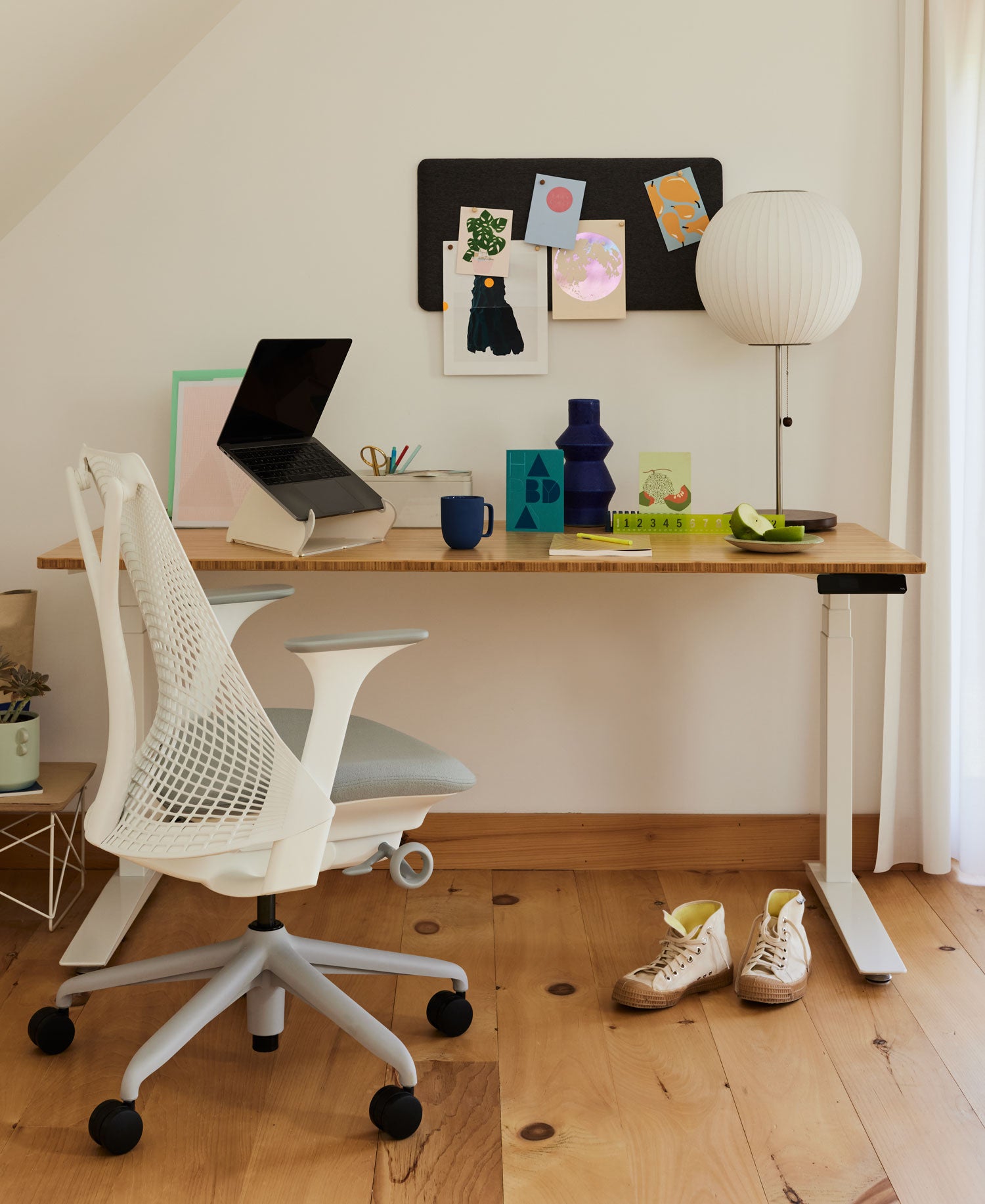 Home office with Sayl office chair with white frame and pale grey sit pad in front office Jarbis sit-stand desk with white frame and hard wood top with laptop on Oripura stand and Nelson bubble table lamp