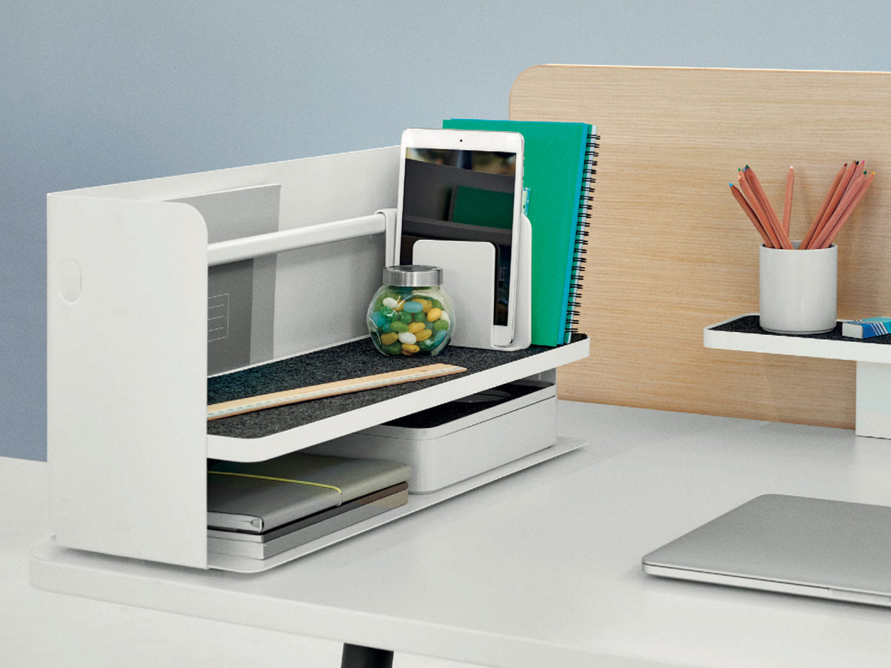 A white Ubi desktop organiser by Herman Miller, placed on the edge of a white desk. Featuring a grey shelf liner, white bookend and a white Formwork stationary box by Herman Miller.