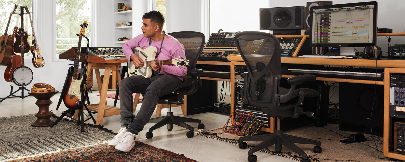 Rostam Batmanglij, musician, producer and composer, in his music studio playing an Italia Modena Electric Sitar guitar sat in Aeron office chair in graphite.
