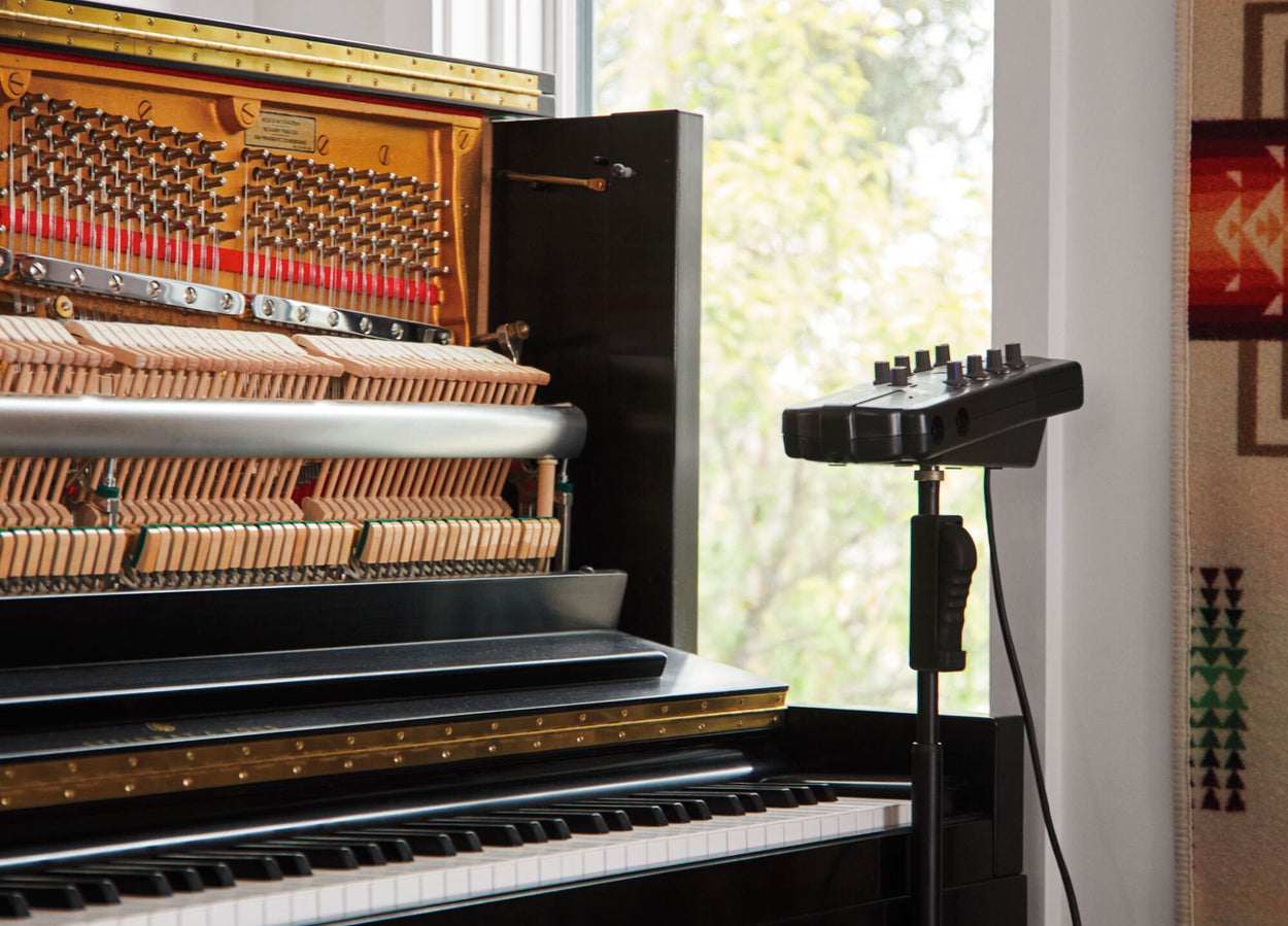 An upright piano with front open with sound recording equipment  next to it.